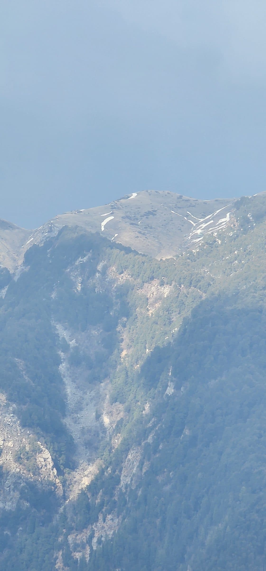 View of forested mountains in Jibhi Valley with patches of snow on the peaks