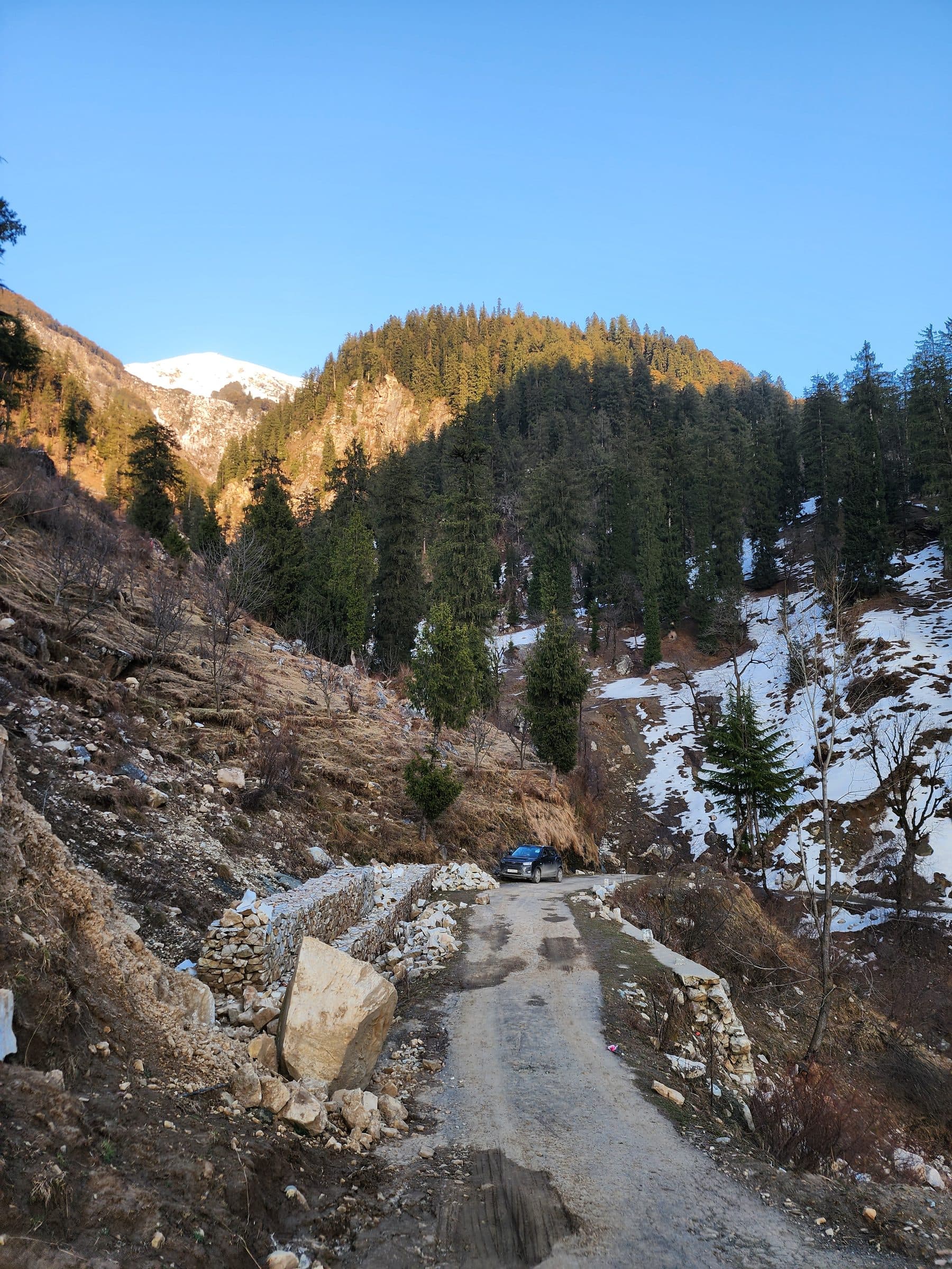 Dirt road winding through dry, rocky hills with sparse trees