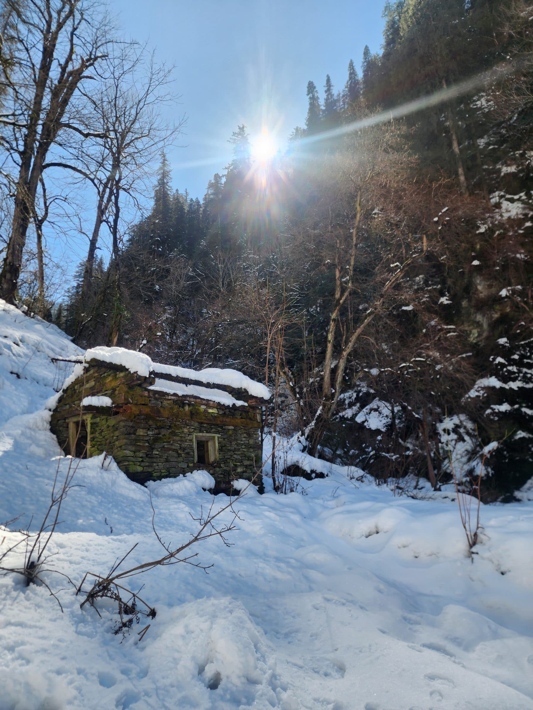 A rustic stone structure surrounded by bare trees in a snowy mountain landscape