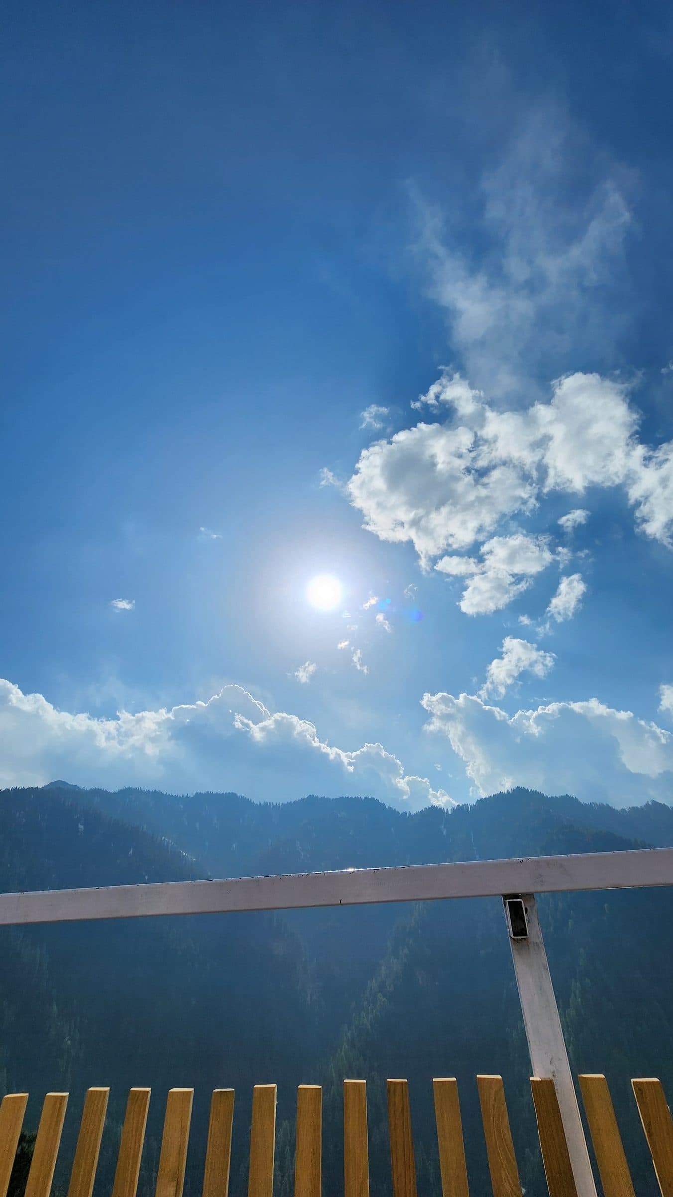 Wooden railing overlooking vast blue sky and distant mountain ranges