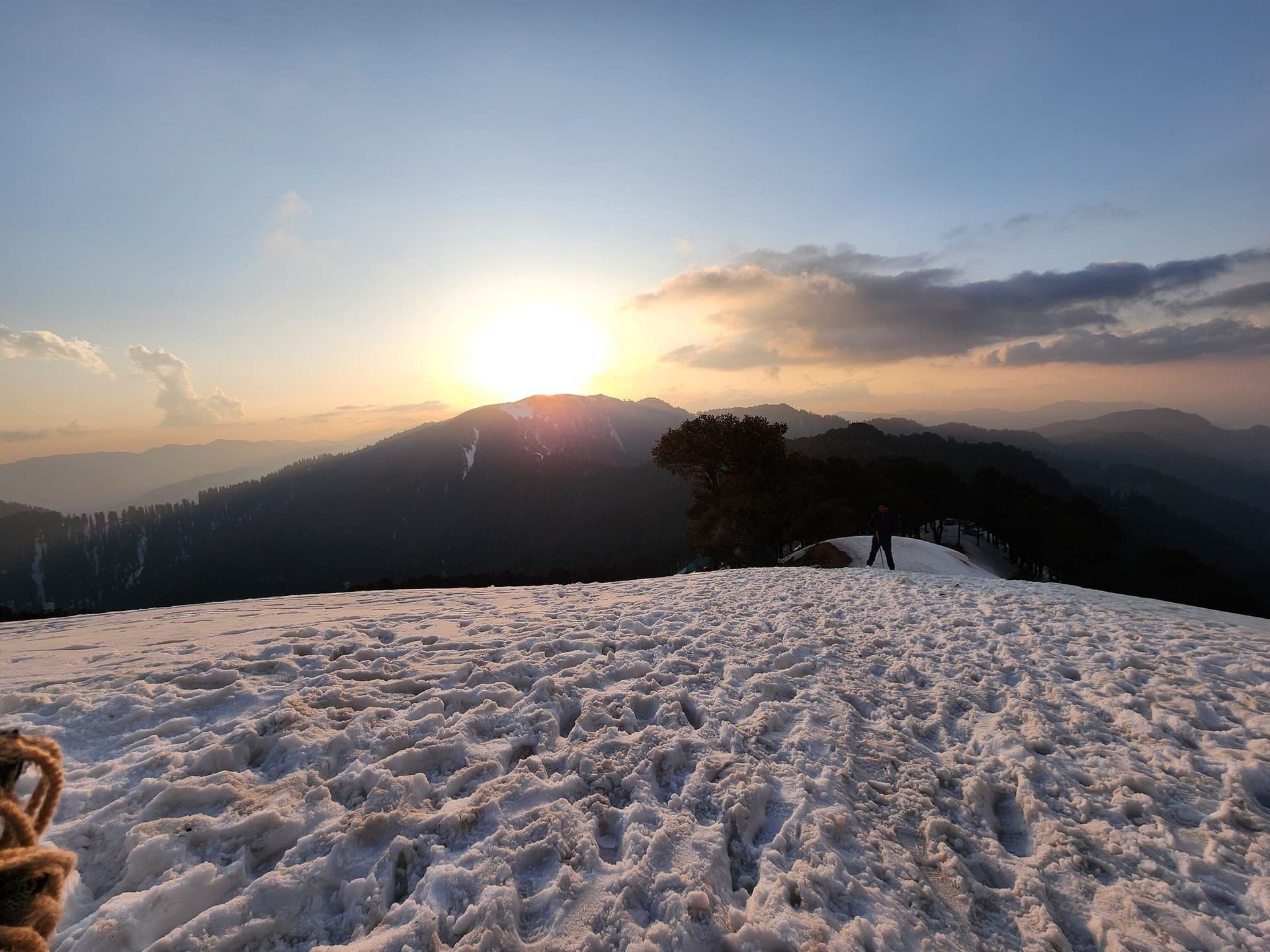 Snow-covered mountains and silhouettes of trees under a bright sky