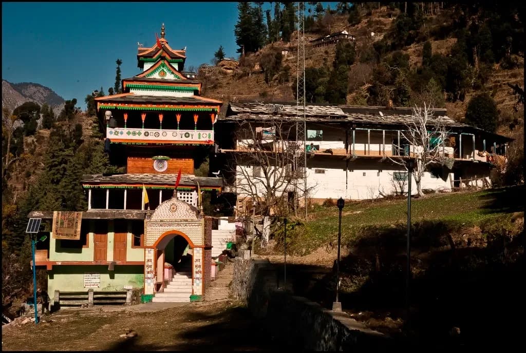 Stone gateway structure leading up to hillside buildings in Jibhi Valley
