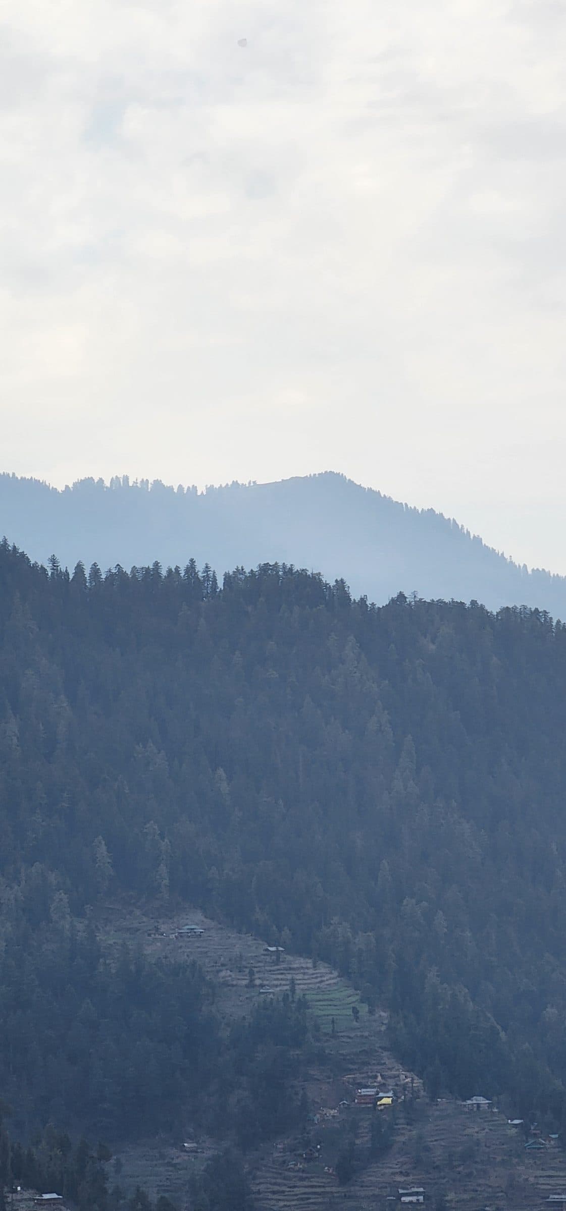 Layered forested mountains with a hazy, misty atmosphere in the valley