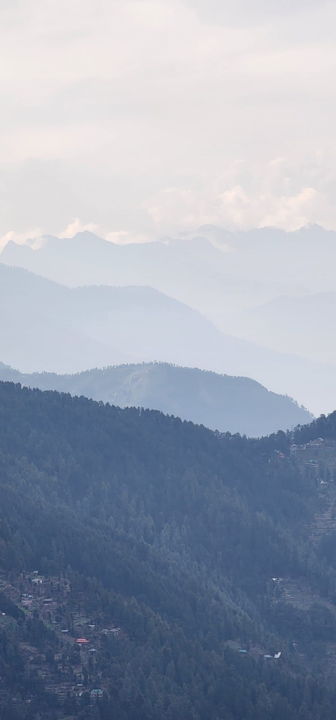 A breathtaking view of a misty mountain valley in Jibhi Shoja, Himachal Pradesh, India, showcasing lush greenery and distant peaks.