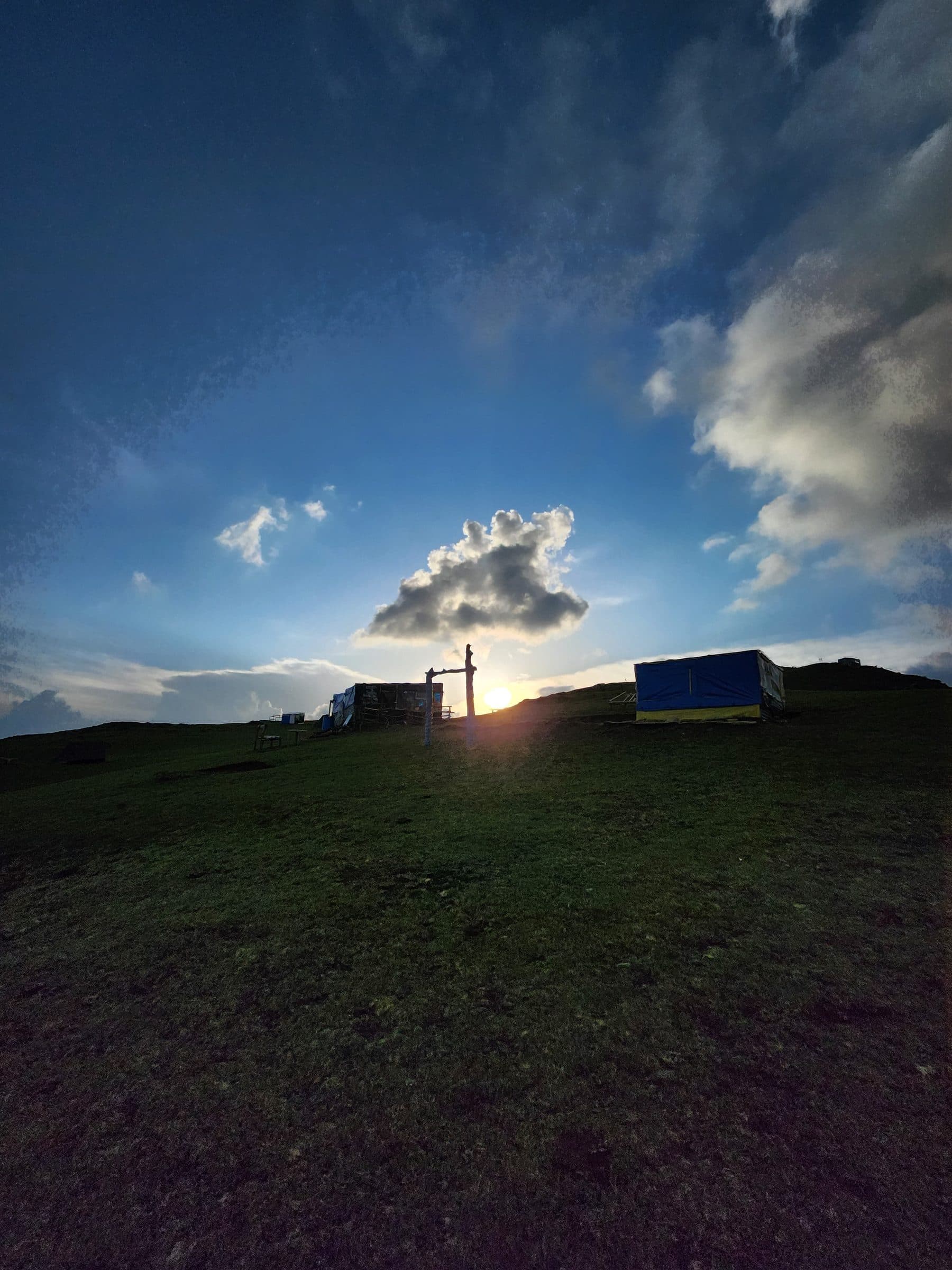 Expansive green hillside under a dramatic cloudy sky in Jibhi Valley