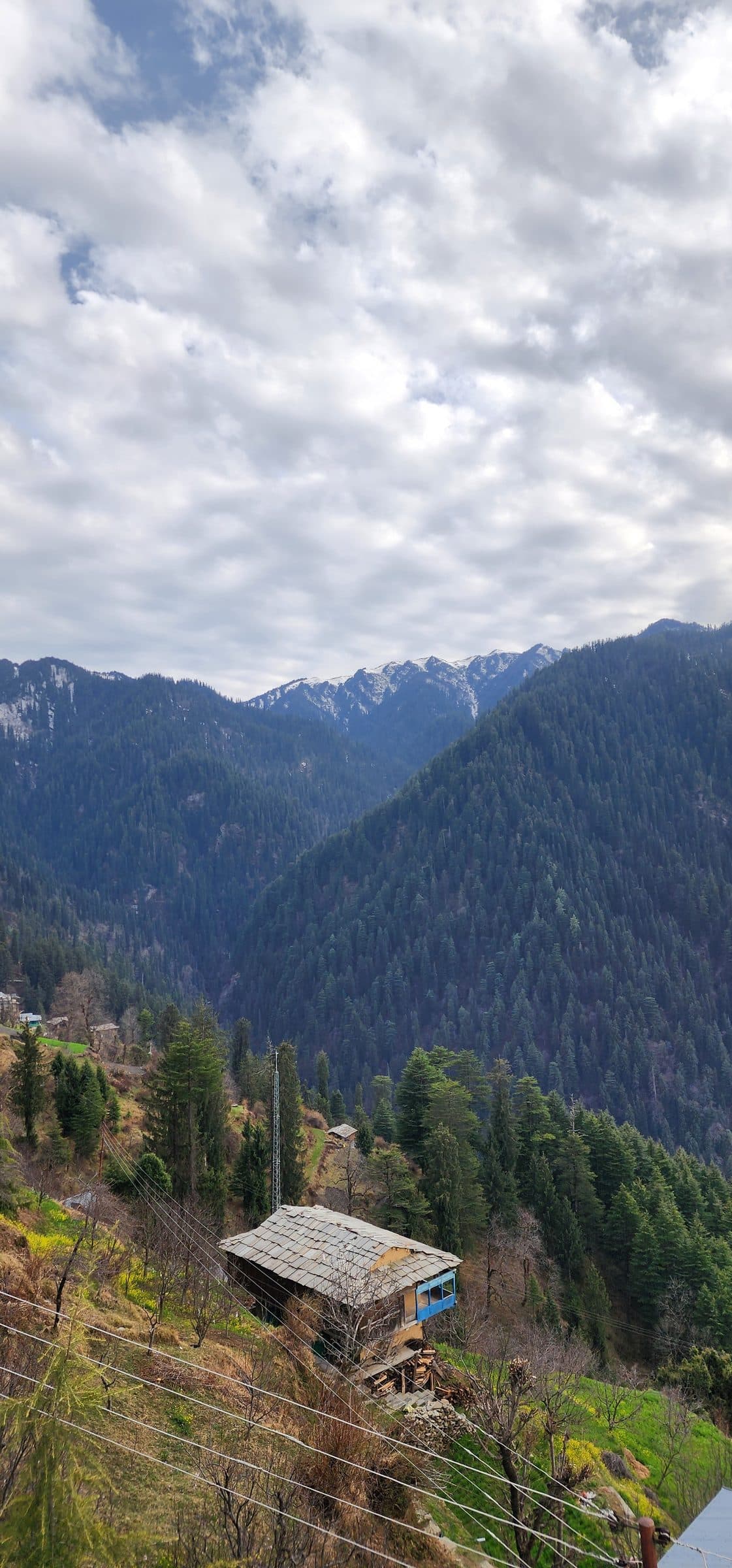View of forested hills and slopes in the Jibhi Valley with cloudy sky