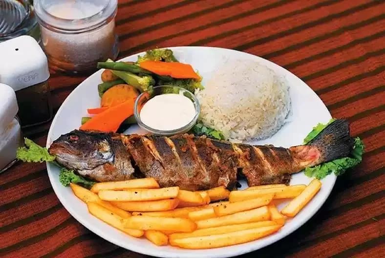 Grilled trout fish, rice, and vegetables served on a mat and in a bowl