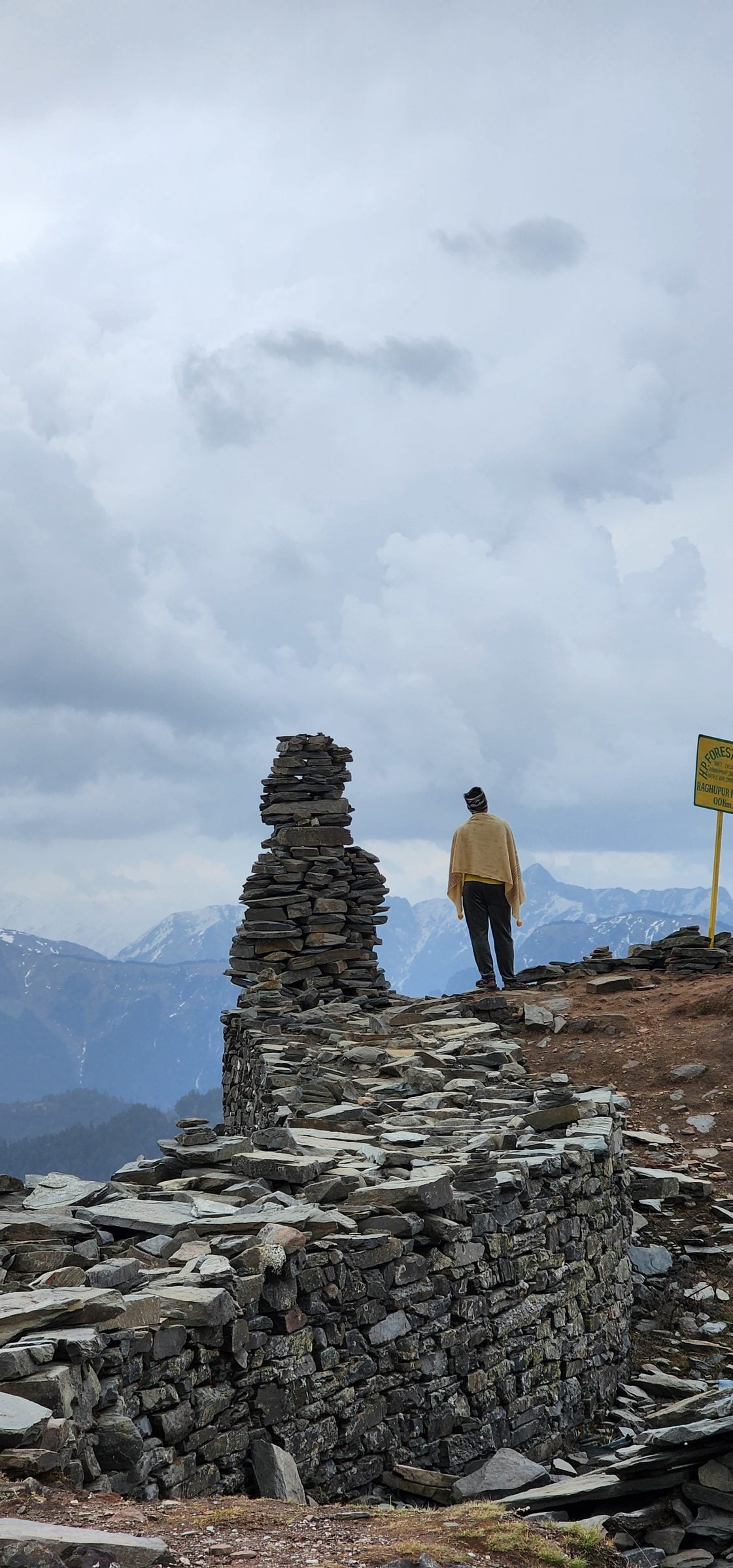 Stone Formation in Jibhi Valley Landscape A person stands near a large stack of grey stones overlooking the mountain valley.
