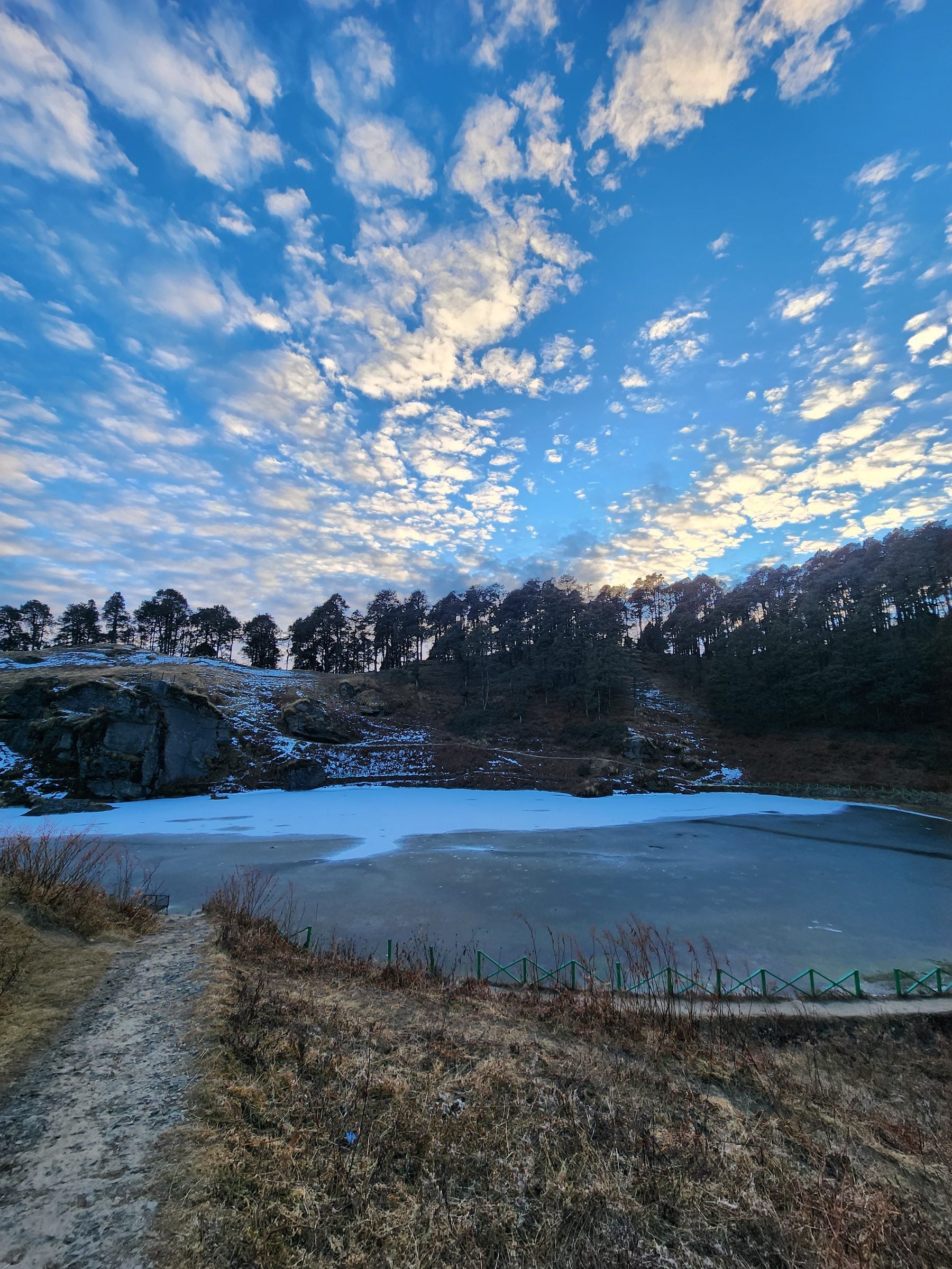 Silent Reflections: Jibhi Valley Winter Serenity A tranquil frozen lake reflects the winter sky above the snow-dusted hills of Jibhi Valley, Himachal Pradesh.