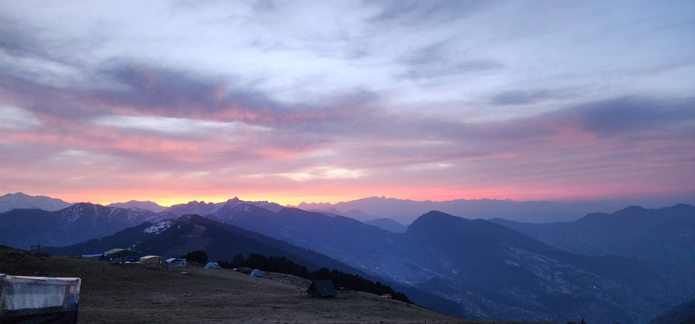 Serene Dawn Over Jibhi Valley, Himachal Pradesh A picturesque view of a campsite nestled amidst the mountains of Jibhi Valley, Himachal Pradesh, with a vibrant pink sunrise.