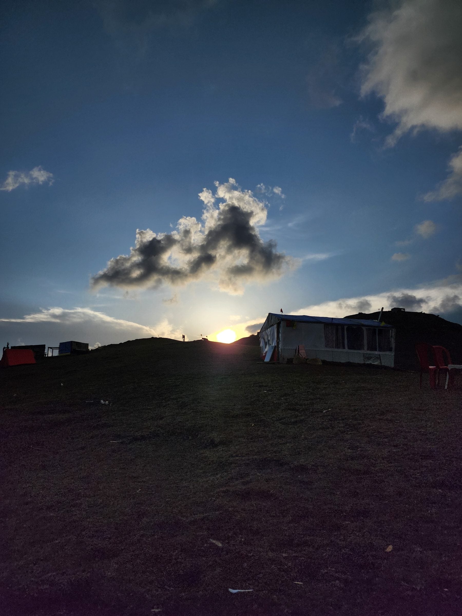 Shoja Valley: A Moment of Serenity in Jibhi A solitary wooden bench sits under a partially cloudy sky in the picturesque Shoja Valley, Himachal Pradesh, India.