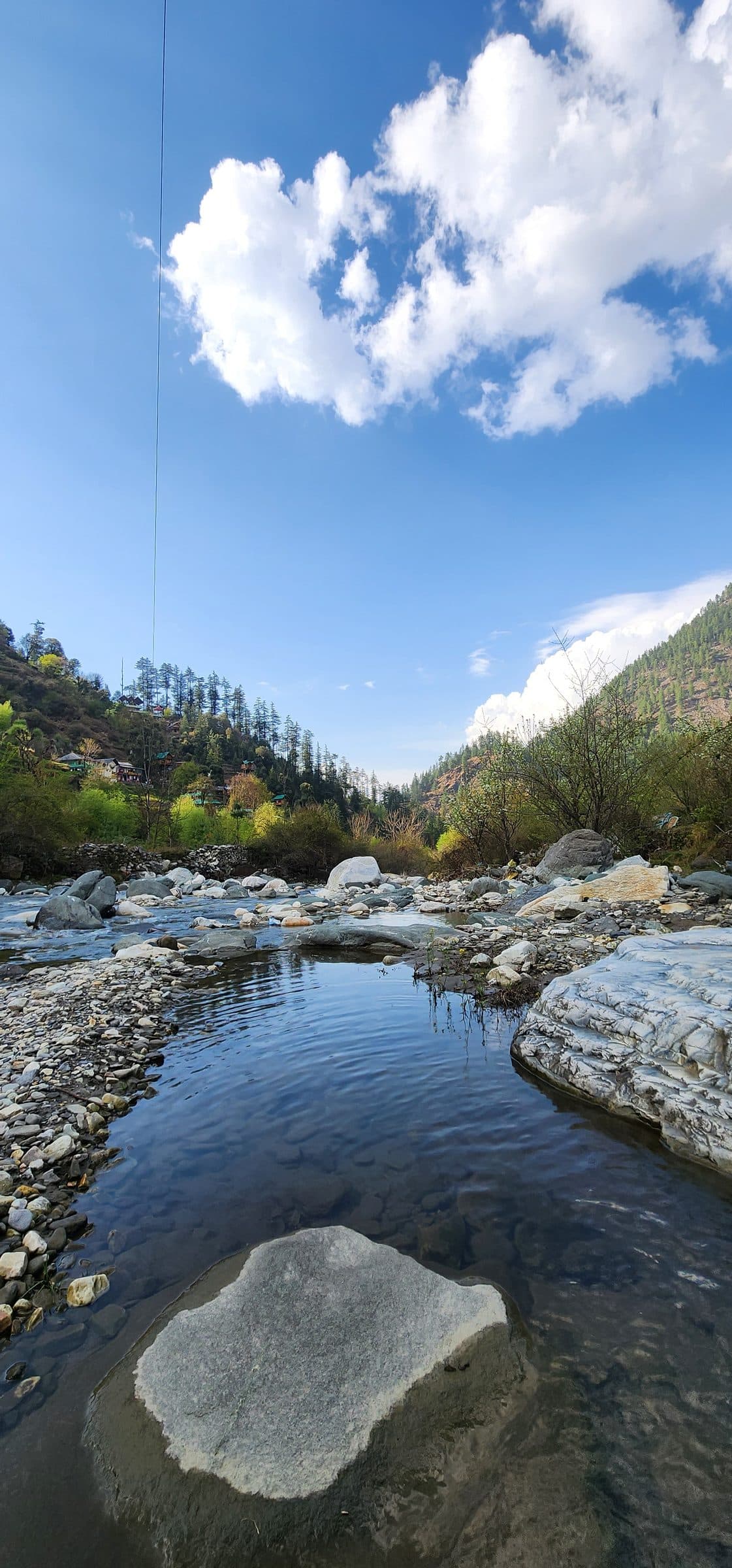 A wide shallow reach of the Tirthan river near Jibhi, smooth boulders and clear pools under a blue sky