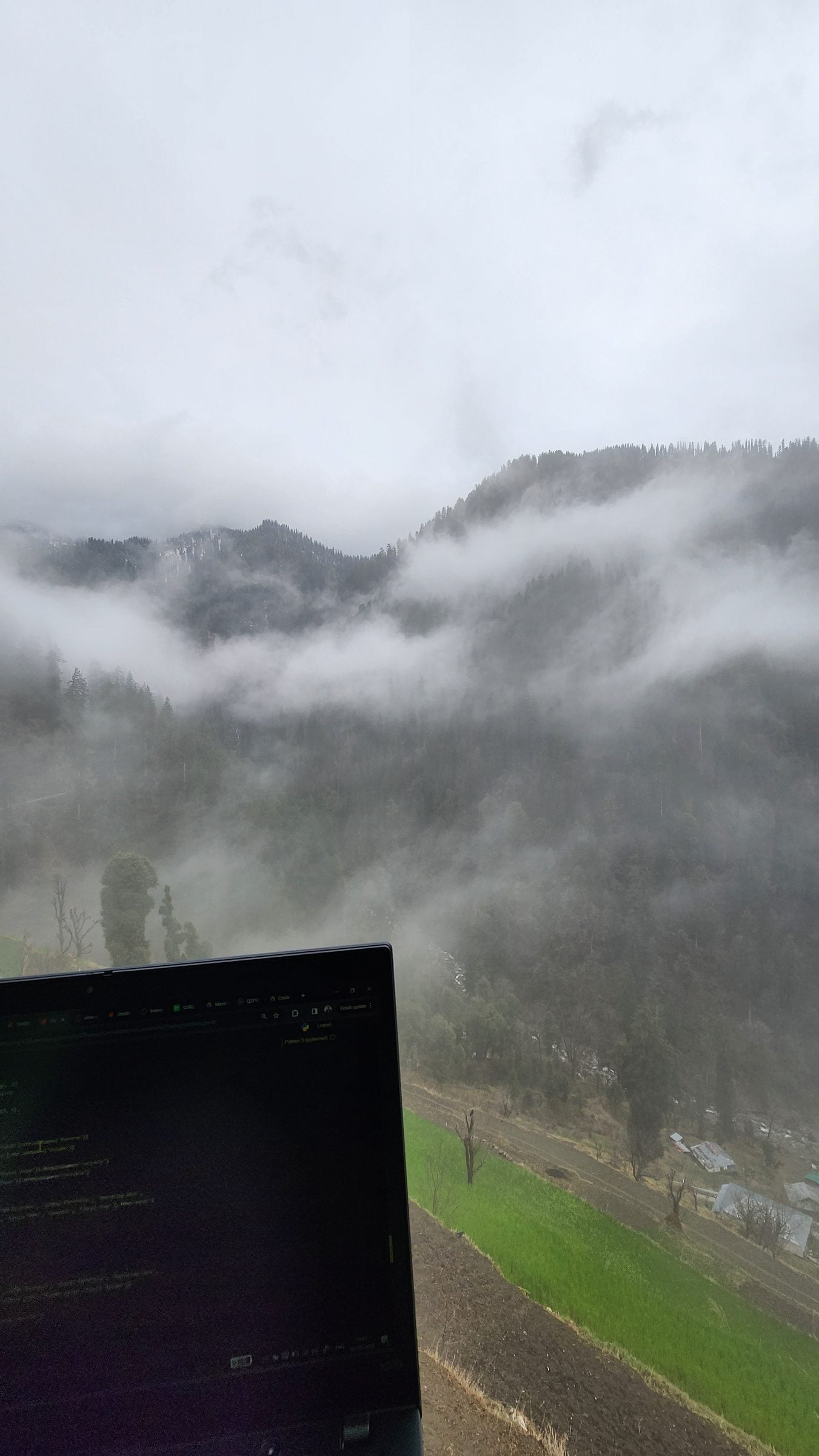 Serene Shoja Valley - Himachal Pradesh, India A laptop rests amidst the rolling hills of Shoja village in Jibhi Valley, Himachal Pradesh, India, showcasing a misty landscape.