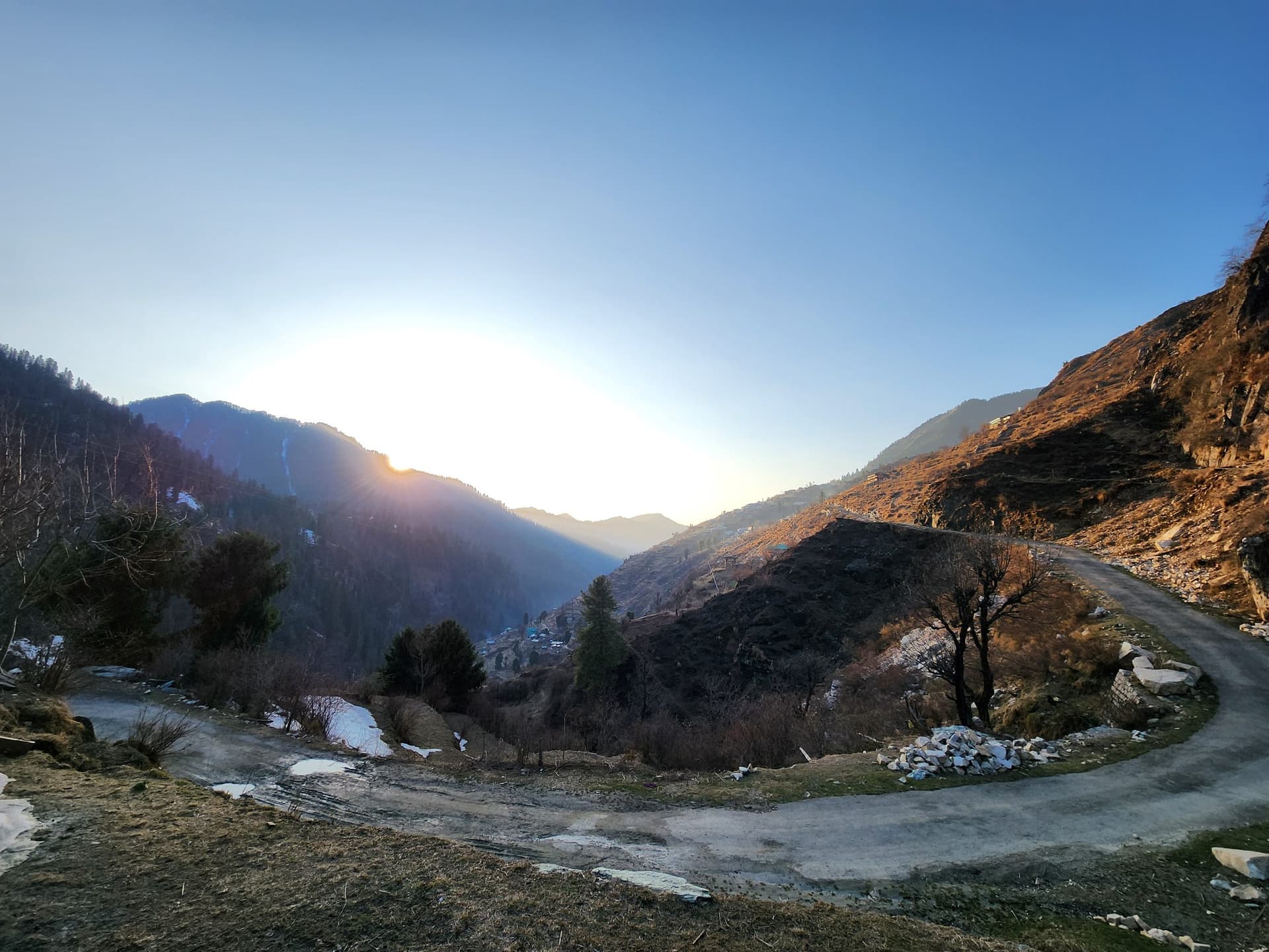A dirt road winds through a dry, scrubby hillside in the Jibhi Valley