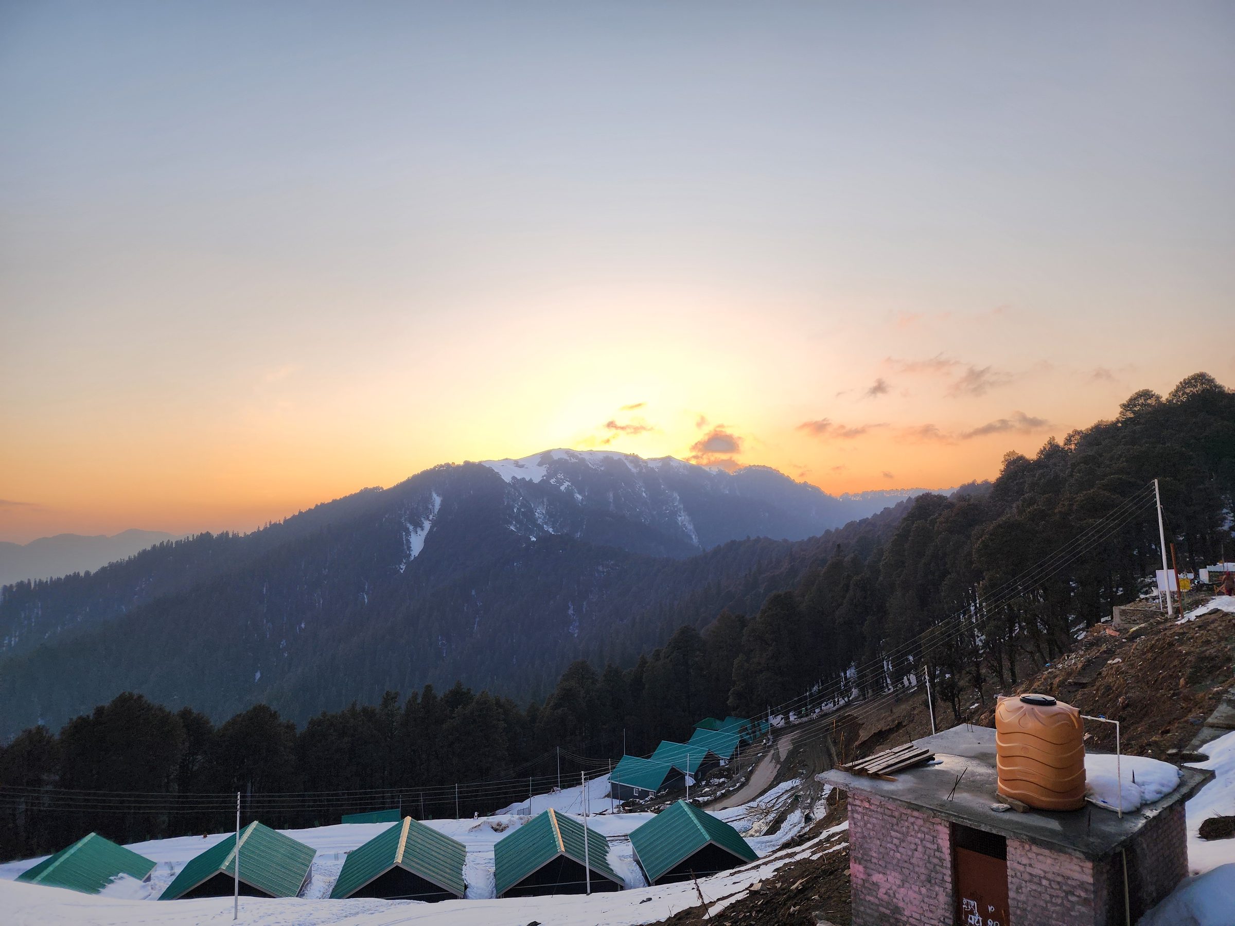 Green-roofed cabins overlooking lush green mountains and forest in Jibhi