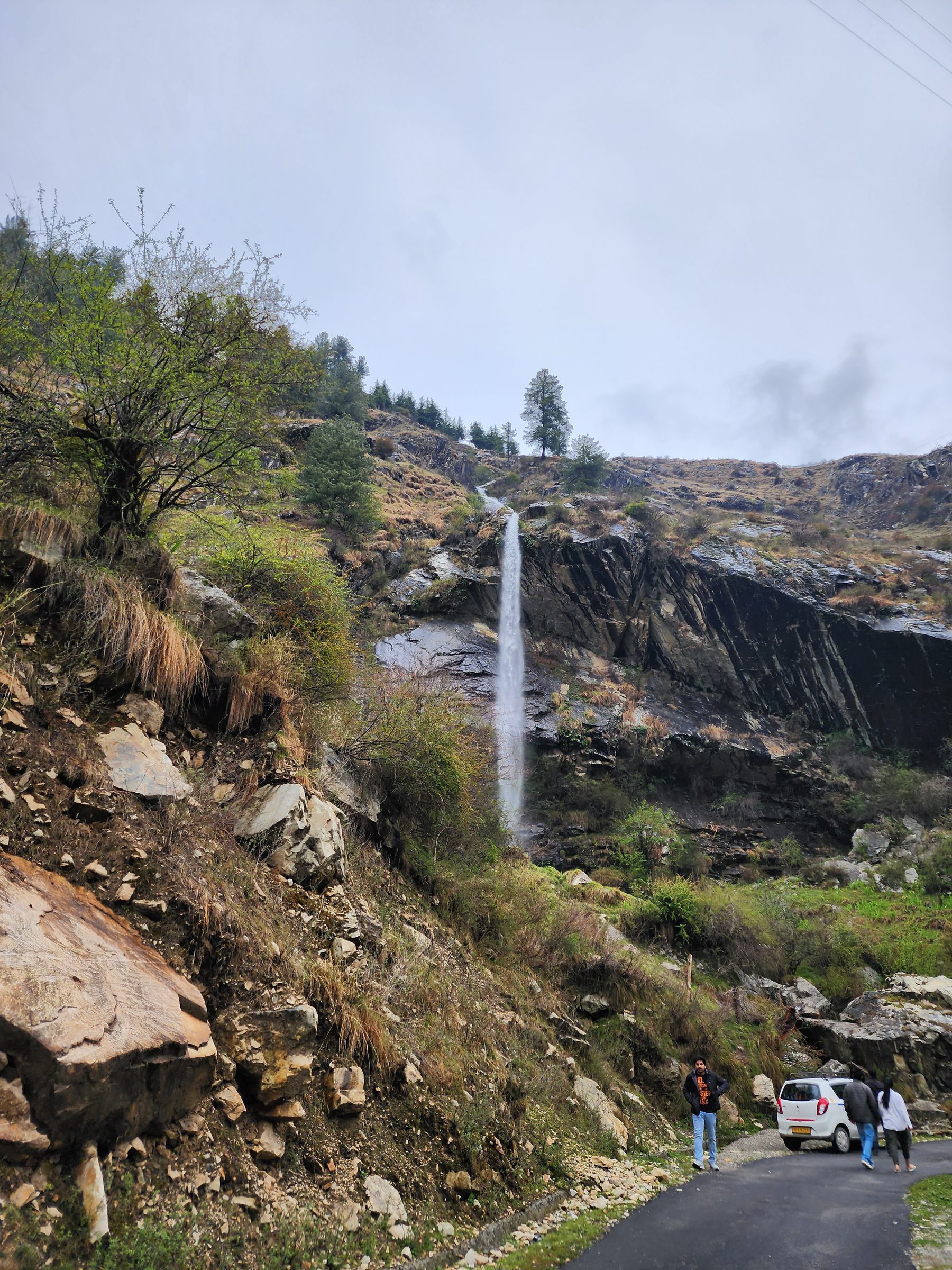A rocky, vegetated hillside with a waterfall and a path in the Jibhi Valley.
