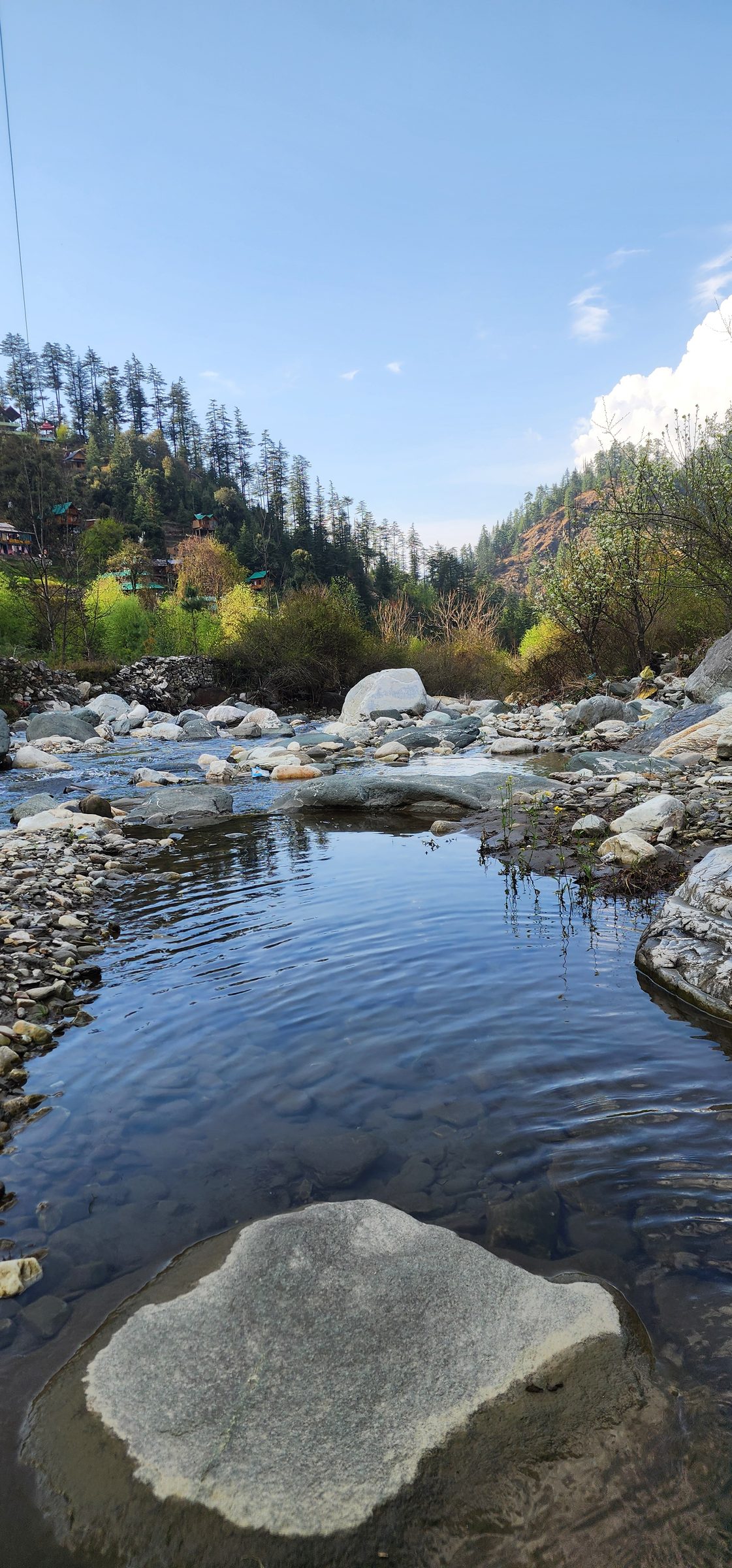 Clear flowing stream over smooth rocks reflecting the blue sky and green foliage, near Ailyak Shoja