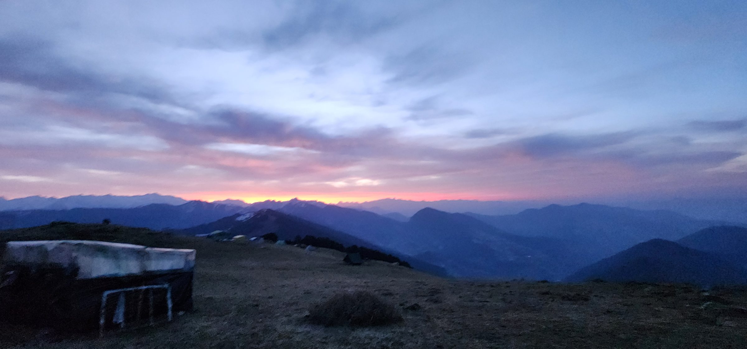 Vast mountain range under a colorful, diffused sky in Jibhi Valley.