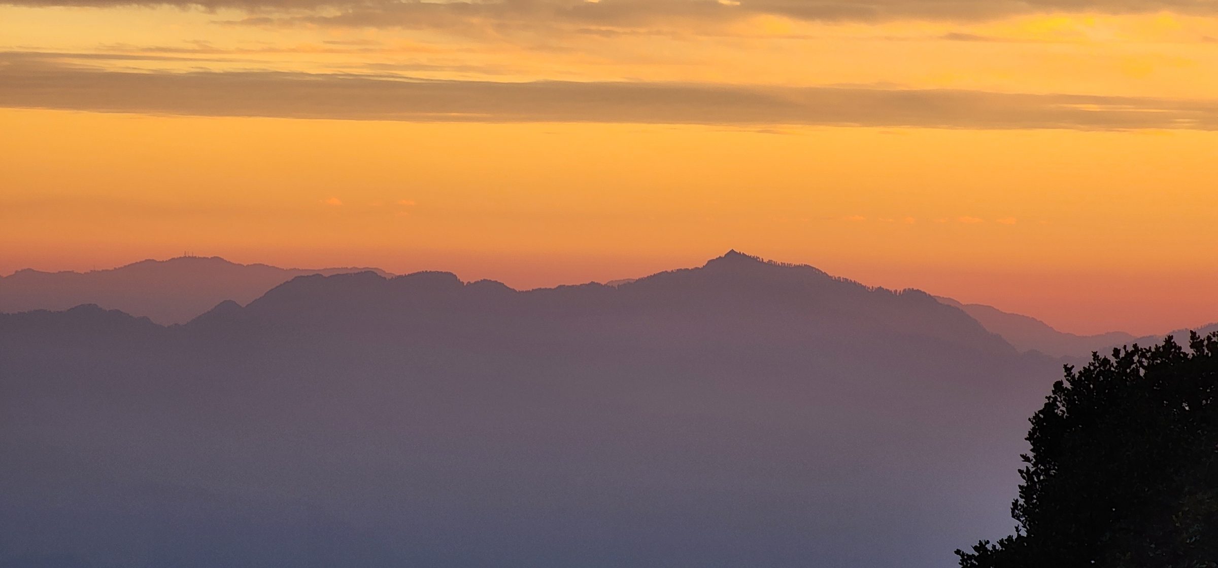 Layered mountain ranges under an orange hazy sky in Jibhi Valley